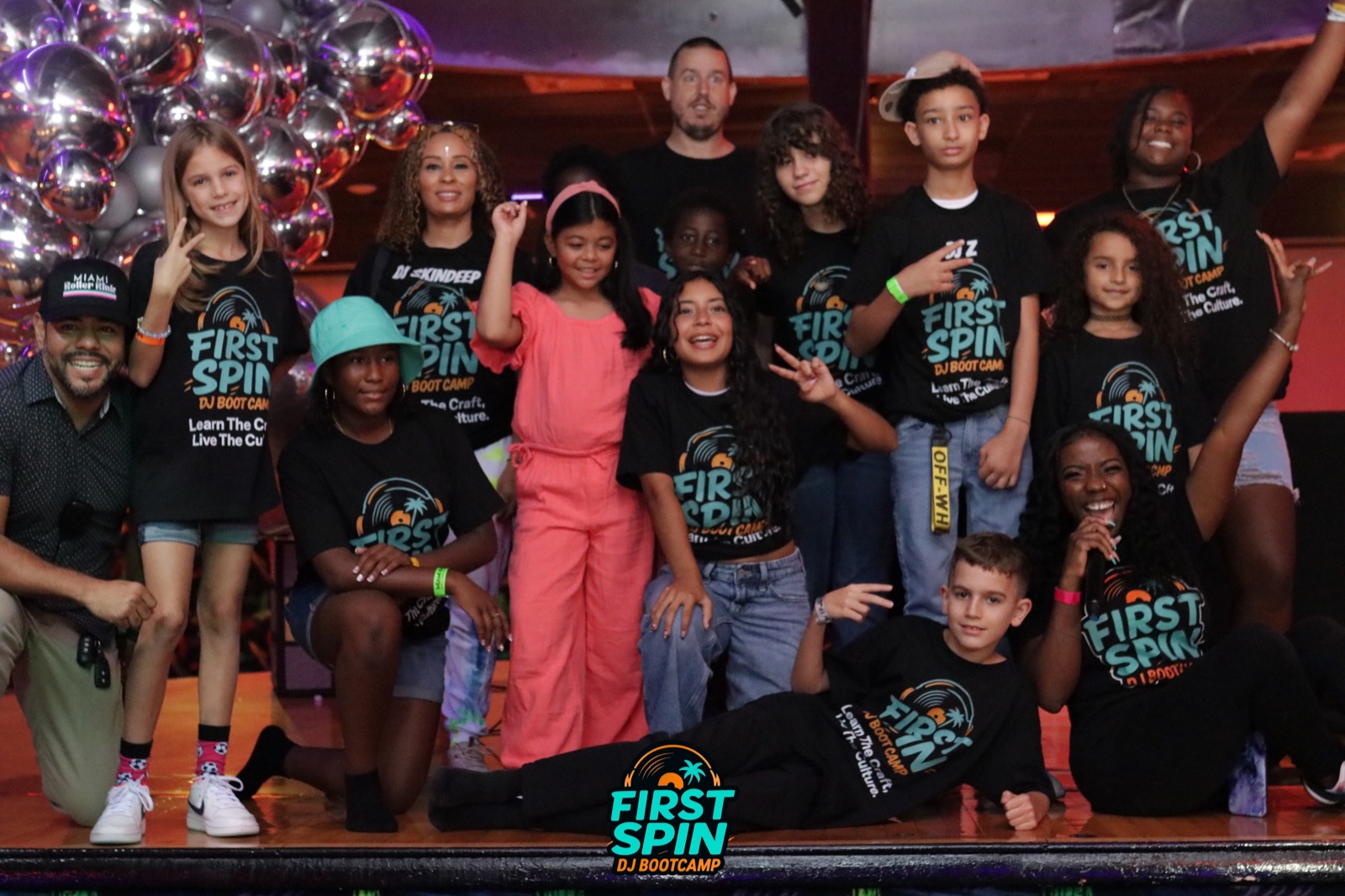 A large, diverse group of First Spin DJ Bootcamp students and mentors celebrating together at a Miami event.
